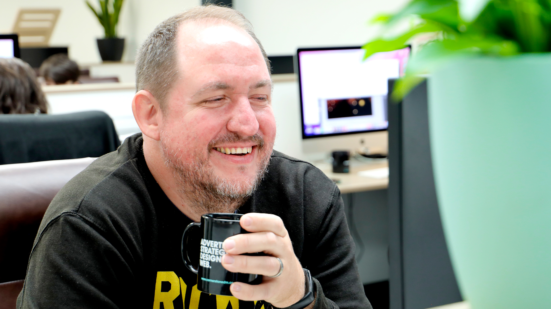 Chris smiling at his desk with a brew