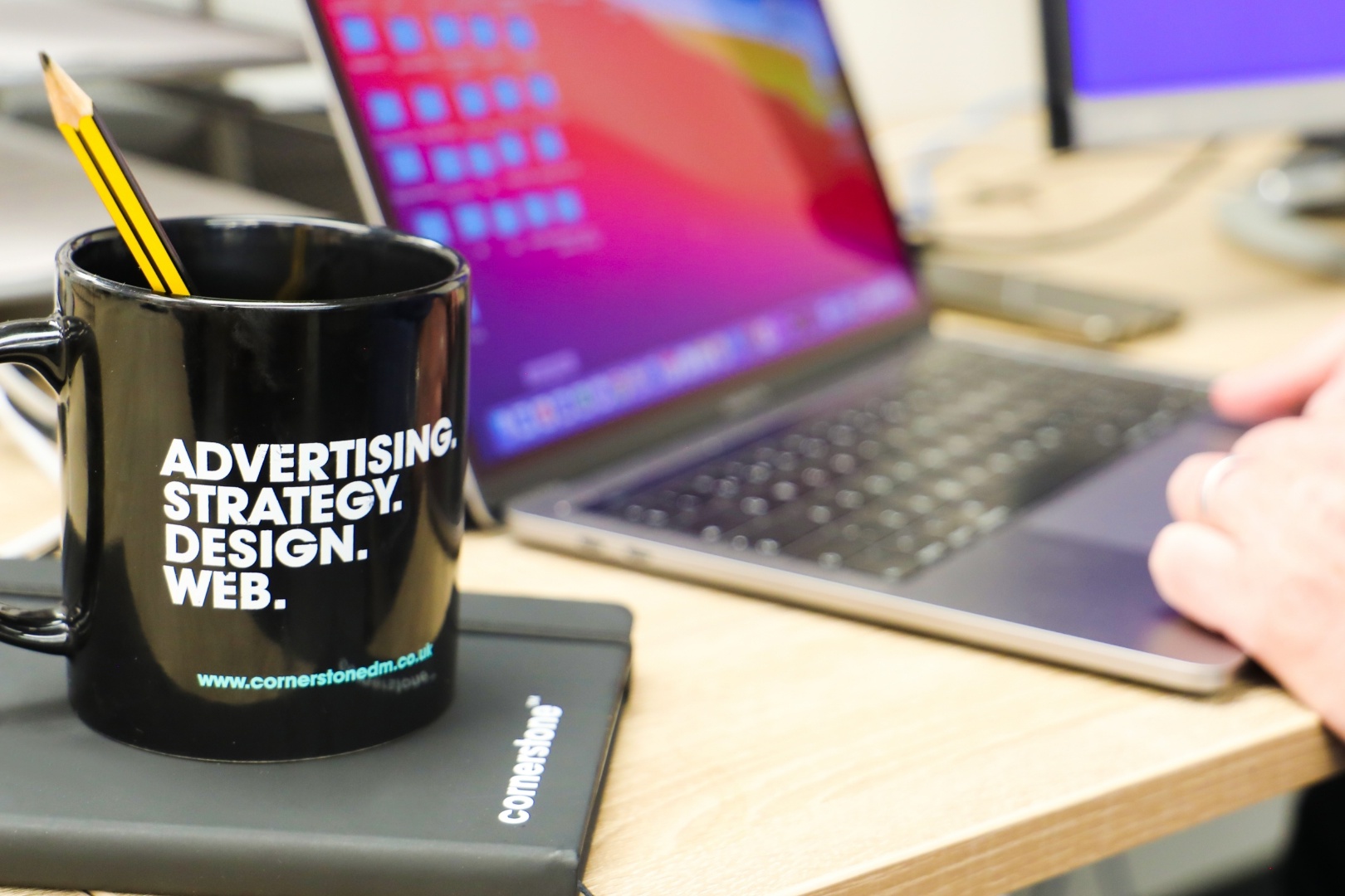 Close up shot of a design team member using a laptop alongside a branded cornerstone mug